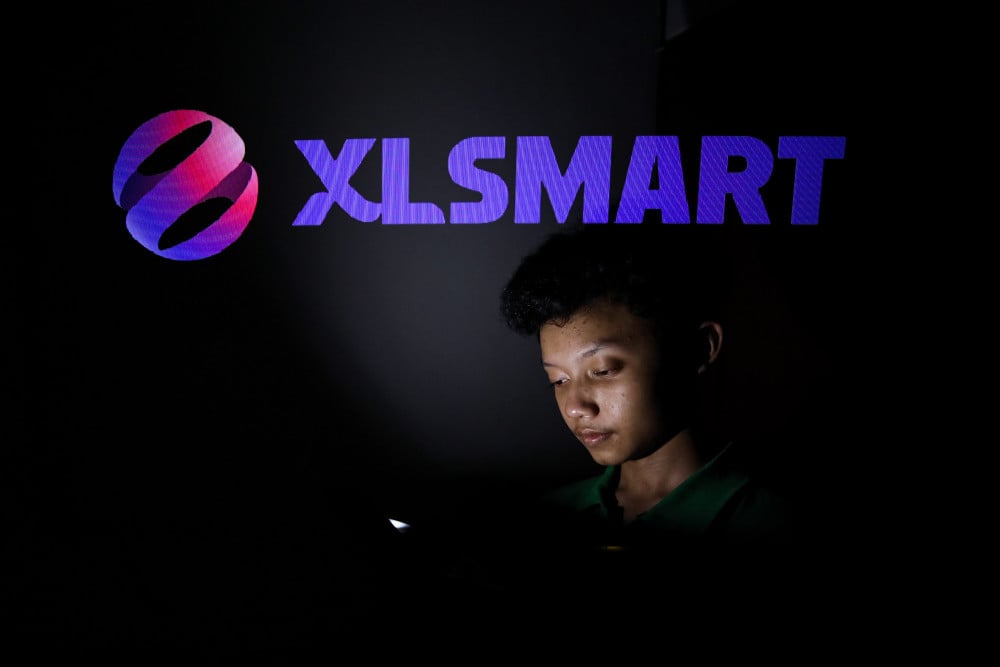 Warga mengakses ponsel di dekat logo XLSmart di Jakarta, Minggu (17/5/2026). Bisnis/Arief Hermawan P